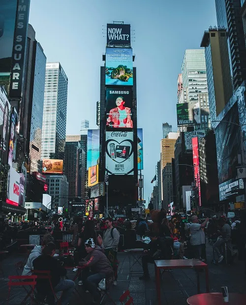 Busy Times Square bustling with people, surrounded by tall buildings and vibrant digital billboards, under a clear blue sky